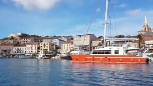 Un puerto con una embarcación naranja grande amarrada, edificios al fondo y un cielo despejado.