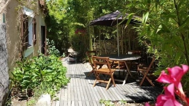 Una terraza de madera con mesa y sillas, rodeada de exuberante vegetación y un sillón colgante.