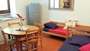 Una habitación compacta con una cama de madera, una mesita con sillas, un escritorio y un refrigerador.