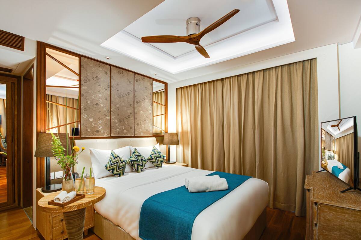 A hotel room with a large bed, a ceiling fan, a bedside table with a lamp, and a mirror.