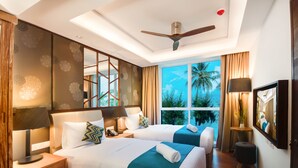 A hotel room with two beds, a ceiling fan, a large window with a view of palm trees, and a small table with a lamp. - Seasalter Maldives (Hulhumalé)