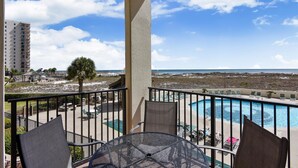 A balcony with a view of a beach and ocean, a pool, and outdoor seating. - Phoenix VII-111 | Beachfront | Resort Style Amenities | My Beach Getaways (Orange Beach)