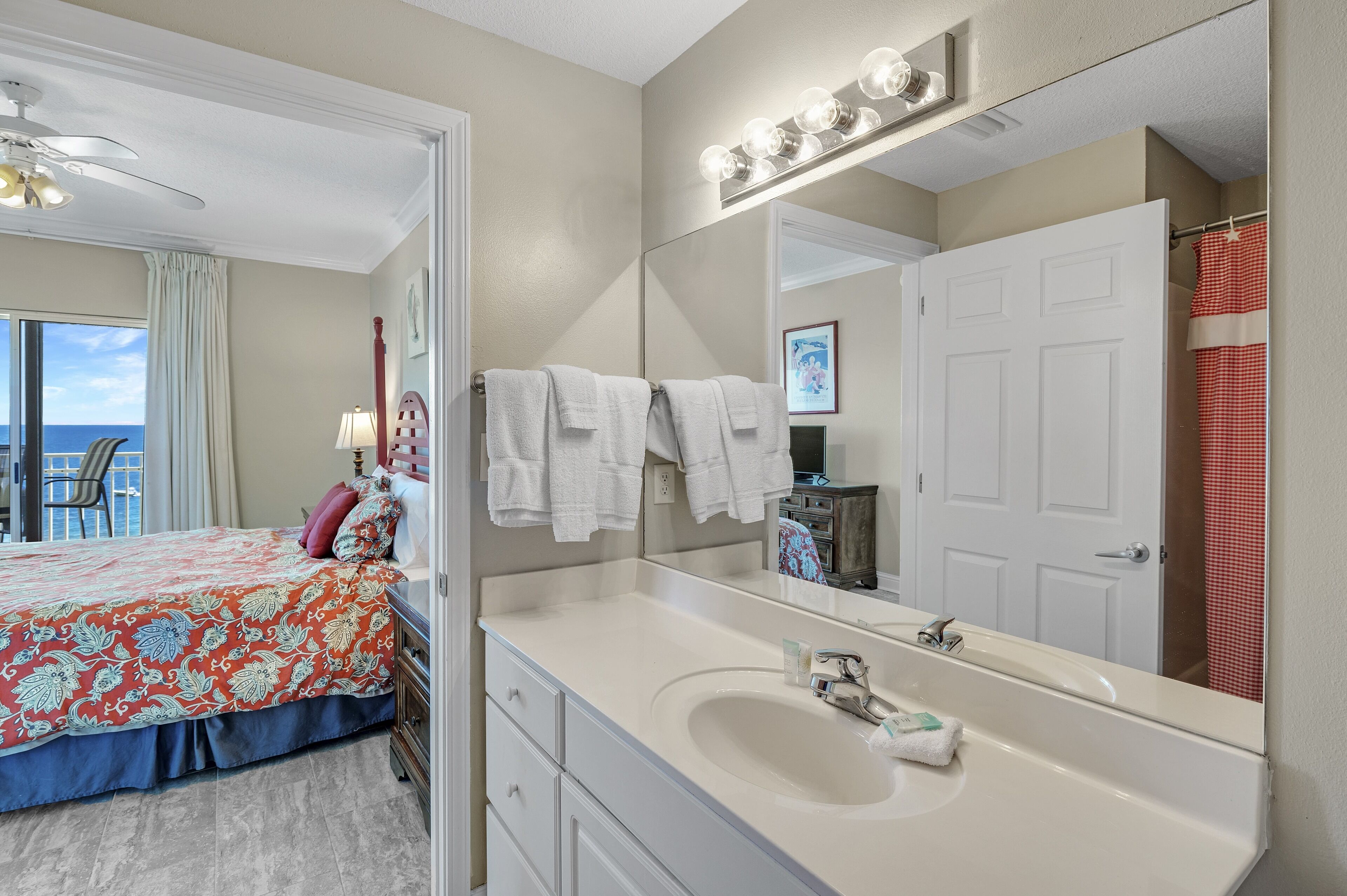 A hotel room with a large bed, a bathroom with a vanity, a mirror, and a view of the ocean.