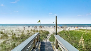 A wooden boardwalk leading to a beach with umbrellas and people.