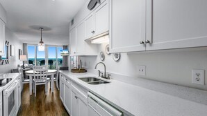 A modern kitchen with white cabinetry, a dining area with a round table and chairs, and a view of the ocean through large windows.