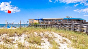 A beachfront property with a wooden deck, a building with a blue roof, and a red flag.