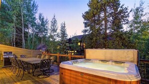 Terraza de madera con jacuzzi, mobiliario exterior y una parrilla.