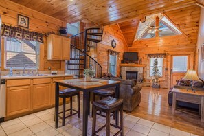 Cozy cabin interior with a central kitchen, seating area, and spiral staircase.