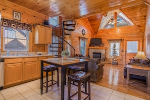 Cozy cabin interior with a central kitchen, seating area, and spiral staircase.