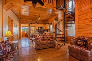 Cozy cabin-style interior with a central living area, dining space, and kitchen, featuring a spiral staircase and natural light.
