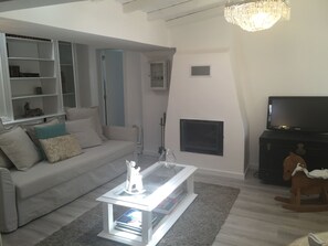 Uma sala de estar com sofá branco, mesa de centro de vidro, lareira, televisão e estante de livros.