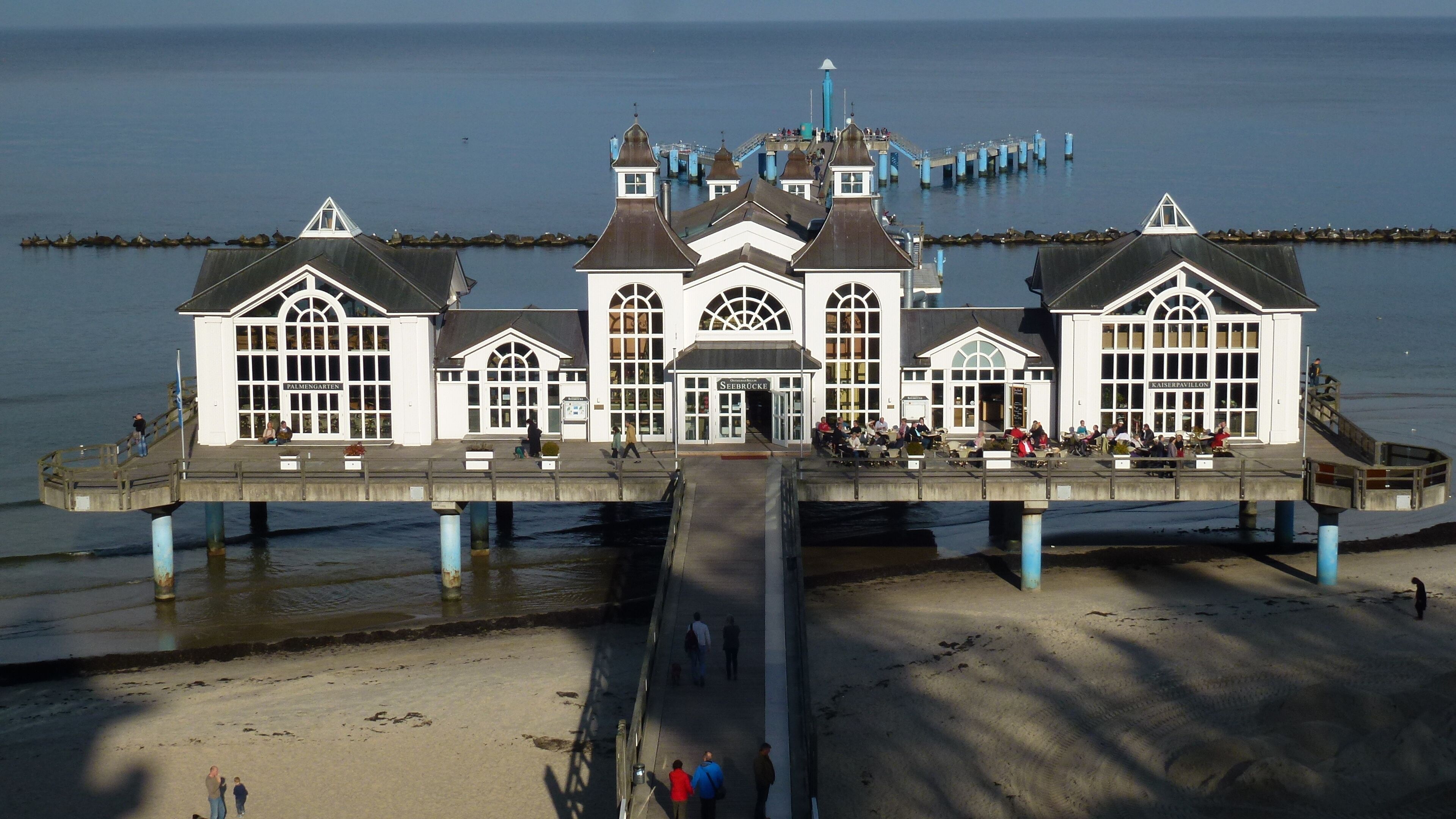 A waterfront building with multiple levels, a central entrance, and a pier extending into the water.