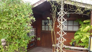 Eine Holzhütte mit einer Holzterrasse, einer Spalierkonstruktion und einer Holztür mit Fenstern.