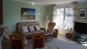 Ein Wohnzimmer mit einer Couch, Sesseln, einem Couchtisch, einem Fernseher und einem Fenster mit Vorhängen.