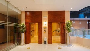 A modern hotel lobby with a glass entrance, wooden paneling, and potted plants.