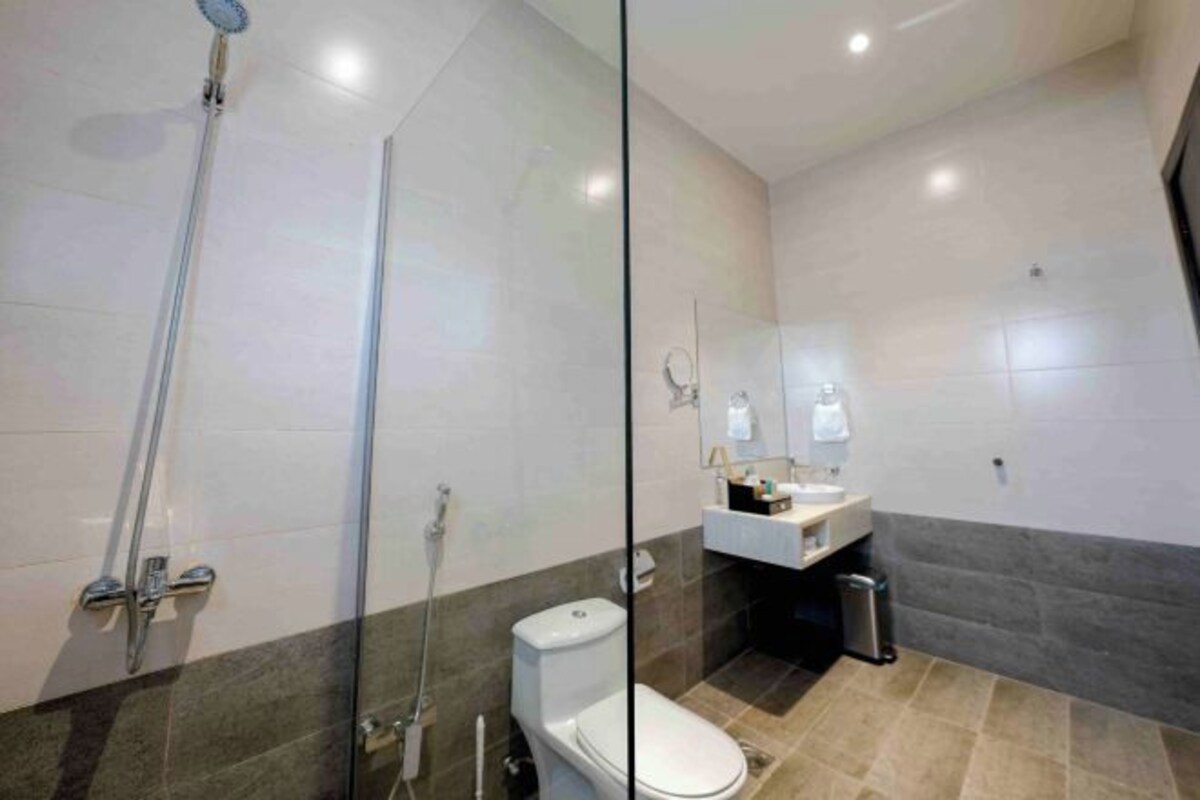 A modern bathroom with a glass shower enclosure, a toilet, a sink with a mirror, and a trash bin.