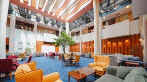 A spacious lobby with multiple seating areas, a central tree, and a high ceiling with a skylight.