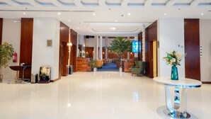 A hotel lobby with a polished floor, wooden paneling, a reception desk, seating area, and a coffee station.