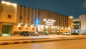 A hotel with a modern facade, a prominent sign, and a parking area with several cars.