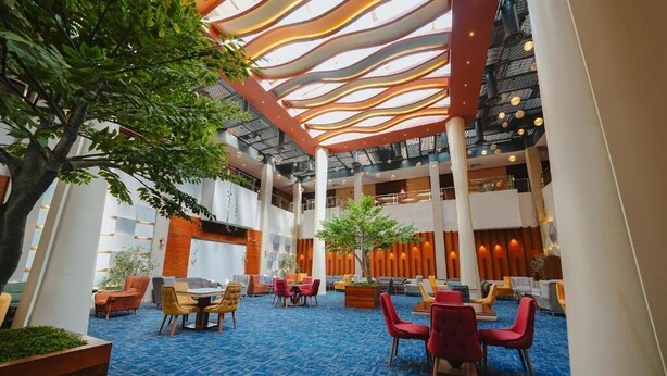 A spacious lobby with a high ceiling, multiple seating areas, and a central plant.