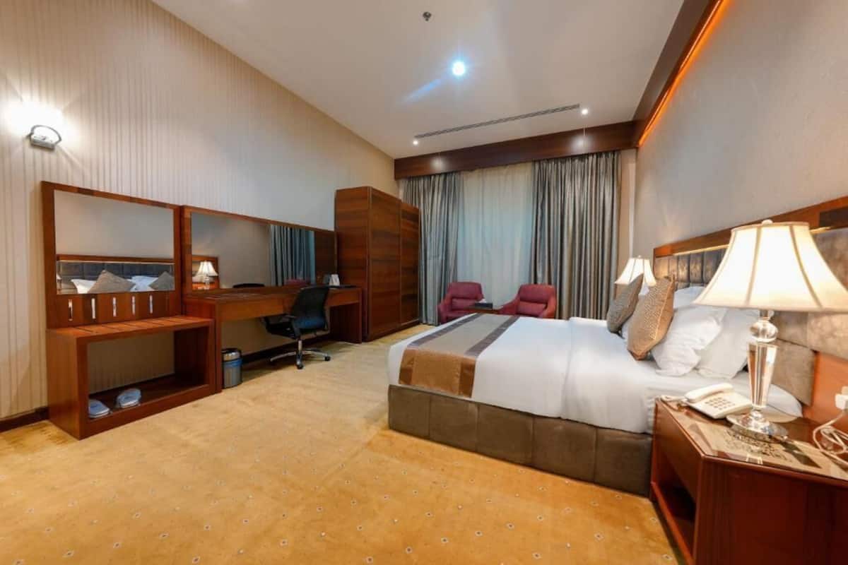 Ein Hotelzimmer mit einem großen Bett, einem Schreibtisch, einem Stuhl, einem Kleiderschrank und einem Spiegel.