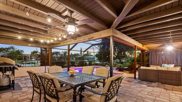 Patio esterno con tavolo e sedie, ventilatore a soffitto e vista sul paesaggio.