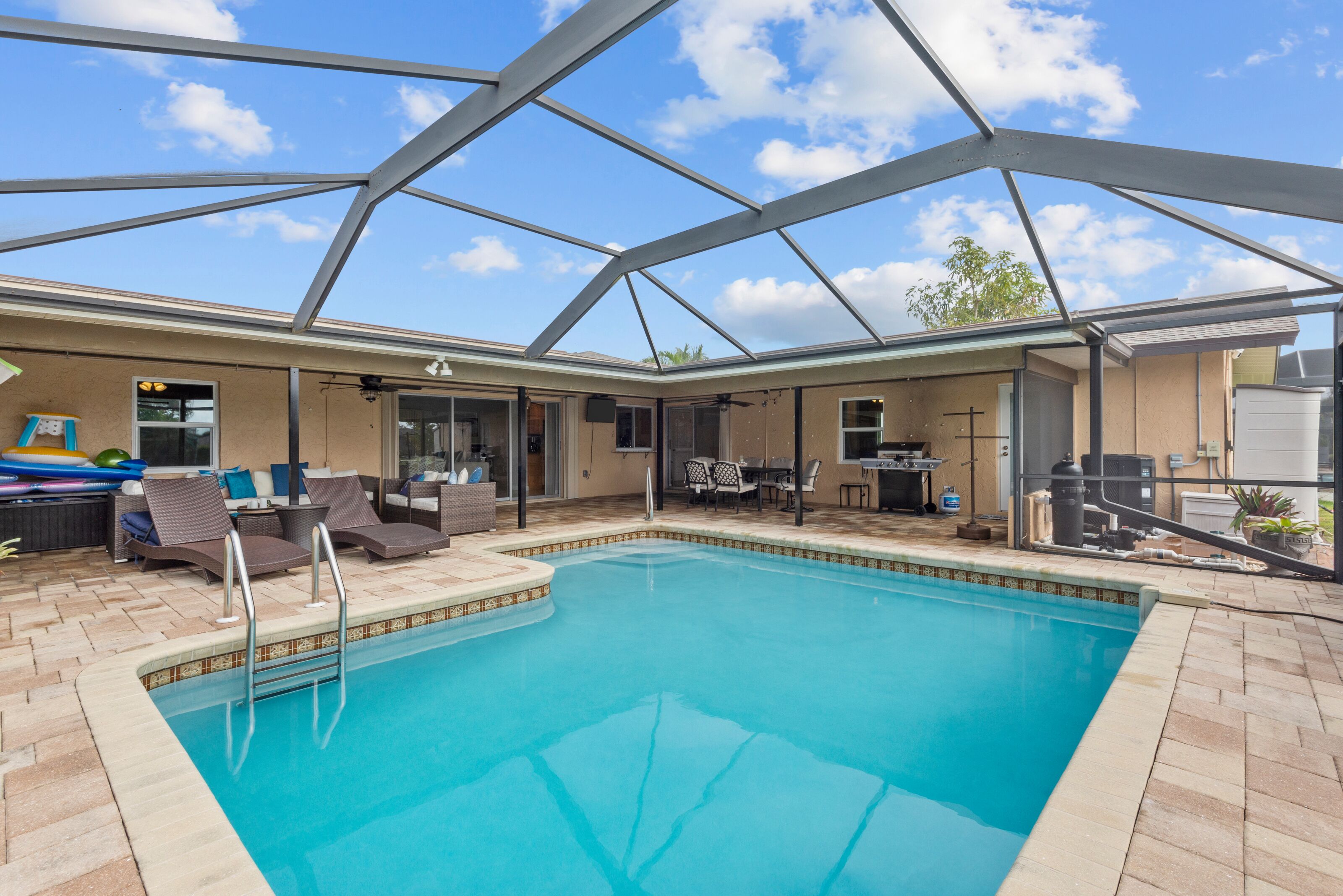 Una piscina interior con techo de vidrio, sillas de descanso y una zona de patio con mesa y sillas.