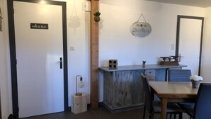 Une pièce avec une porte en bois portant l’inscription « salle de bain », une petite table avec des chaises, un coin bar avec une balance, et une enseigne suspendue sur laquelle on peut lire « König Ilserer ».