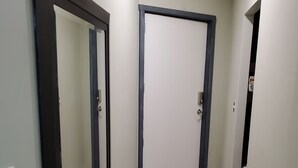 A hallway with two doors, one with a dark frame and the other with a light frame, leading to a room.