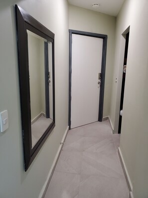 A hallway with two doors, one with a dark frame and the other with a light frame, leading to a room.