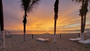 A beach with white lounge chairs and a rope barrier.