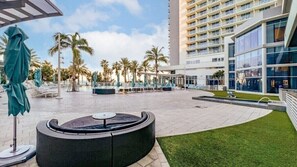 Une cour d’hôtel avec un espace de repos circulaire, des palmiers et un bâtiment moderne doté de balcons.