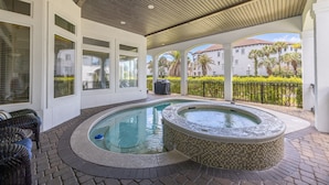 A covered outdoor swimming pool area with a hot tub, wicker furniture, and a view of a residential building. - Private Pool-Golf Cart-Beach Service (Destin)