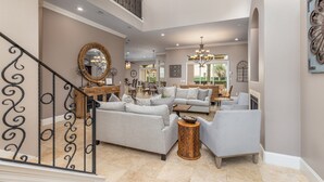 A spacious living area with a staircase, multiple seating arrangements, and a chandelier. - Private Pool-Golf Cart-Beach Service (Destin)