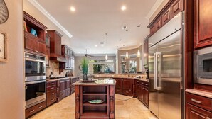 A spacious kitchen with dark wooden cabinets, stainless steel appliances, and a central island. - Private Pool-Golf Cart-Beach Service (Destin)
