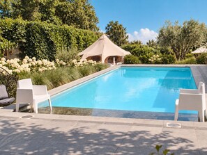 Ein Schwimmbecken mit Liegestühlen, umgeben von viel Grün und einer Zelthalle.