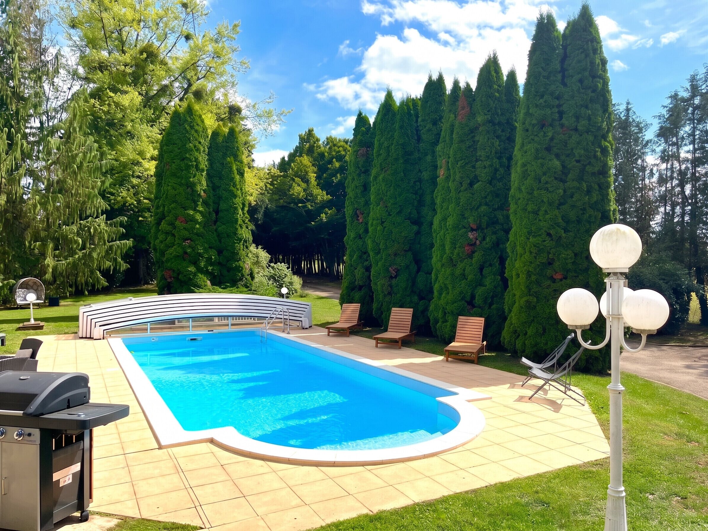 A swimming pool with a curved edge, surrounded by a patio with lounge chairs and a barbecue grill.