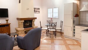 A living room with a fireplace, a dining table with chairs, a television, and a kitchen area with cabinets and a refrigerator.