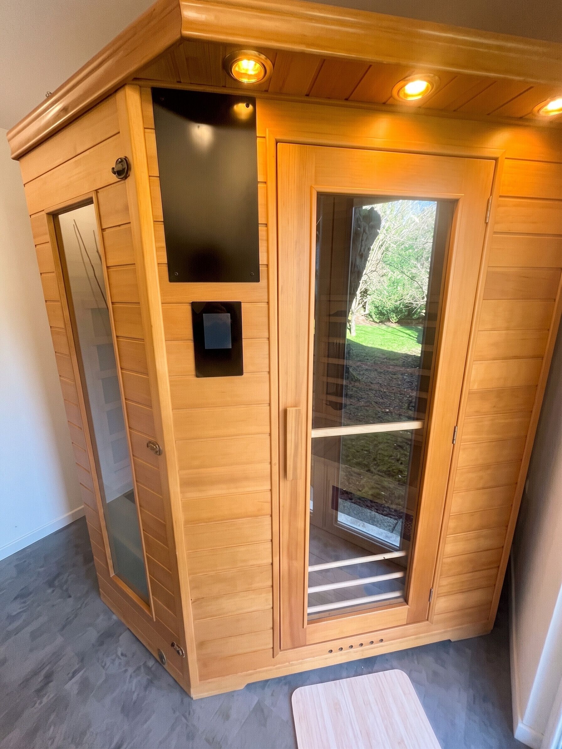 A sauna with a wooden exterior, a glass door, and a small control panel.