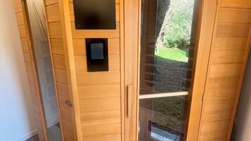 A sauna with a wooden exterior, a glass door, and a small control panel.