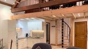 A modern interior with a kitchen, dining area, and a loft bedroom with a wooden staircase.