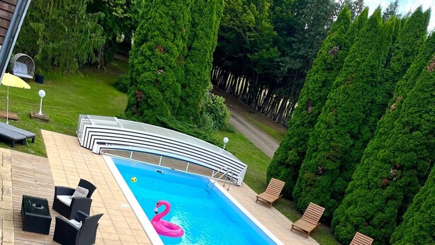 Suorakaiteen muotoinen uima-allas, jossa on vaaleanpunainen flamingo-uimapatja, ja sen ympärillä on terassi, jossa on ulkokalusteita ja grilli.