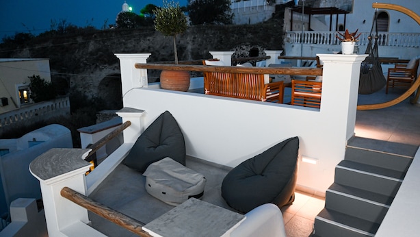 Eine Dachterrasse mit weißer Brüstung, grauen Kissen und einer Holzbank.