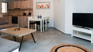 Ein gemütlicher Wohnbereich mit Küchenzeile, Essbereich, einer Couch, einem Couchtisch und einem Fernseher auf einem Schrank.