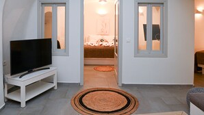 Ein Zimmer mit einem Fernseher auf einem weißen Schrank, einem Teppich auf dem Boden und einer Tür zu einem Schlafzimmer mit einem Bett und einem Nachttisch.