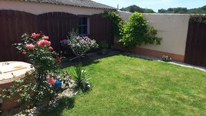 Un jardin à l’arrière de la maison, avec une clôture en bois, une pelouse et diverses plantes et fleurs.