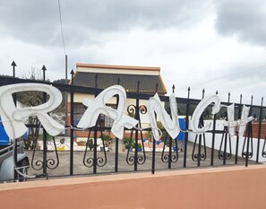A metal fence with large white letters spelling "RANG" and a traditional building in the background. - Magnificent RANCH LAU & RI (Cela velha)