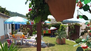 Une clôture en bois agrémentée de jardinières suspendues, un espace patio avec des chaises et une table, et un jardin avec différentes plantes, le tout sur fond d’une autre clôture en bois.