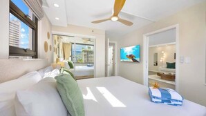 Une chambre d’hôtel avec un lit, un ventilateur de plafond, une télévision et une vue sur la ville par la fenêtre.