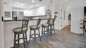 Una cocina moderna con armarios blancos, electrodomésticos de acero inoxidable y una zona de bar con taburetes.